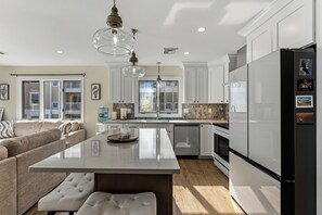 A modern kitchen with white cabinets, a large island, and a black refrigerator. - Oceanview 3BR Condo with Balcony & Seawall Access (North Wildwood)