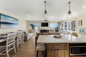 A spacious living area with a large island, a dining table with chairs, a sofa, and a television. - Oceanview 3BR Condo with Balcony & Seawall Access (North Wildwood)