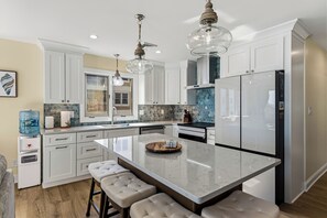 A modern kitchen with white cabinets, a marble island, and pendant lighting. - Oceanview 3BR Condo with Balcony & Seawall Access (North Wildwood)