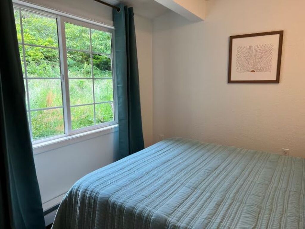 A bedroom with a bed, a window with curtains, and a framed picture on the wall.