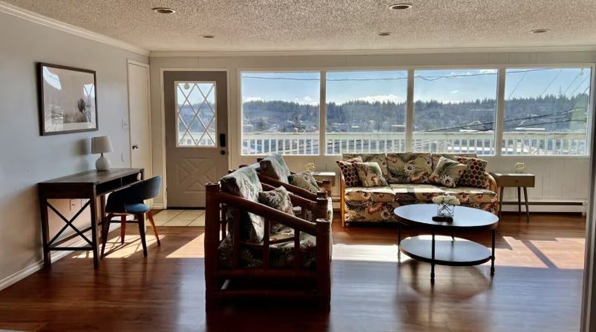 A spacious living room with a large window, a sofa, a chair, and a small table.