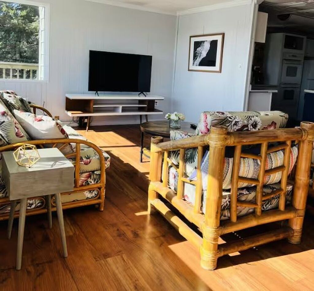 Una sala de estar con televisión, muebles de mimbre y una cocina al fondo.