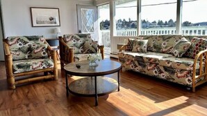 A room with a wooden floor, a round coffee table, two armchairs, a sofa, and a large window with a view.