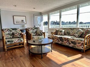 Ein Zimmer mit Holzboden, einem runden Couchtisch, zwei Sesseln, einem Sofa und einem großen Fenster mit Blick.