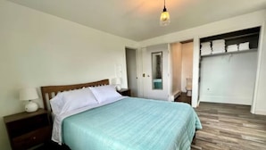 A bedroom with a bed, a nightstand, a lamp, a wardrobe, and a mirror.