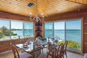 Ein Essbereich mit einem Glastisch, Holzsesseln und Blick auf das Meer.