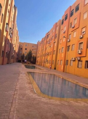 A narrow urban street with multi-story buildings, a central water feature, and a clear sky. - Elegance & Serenity (Marrakech)