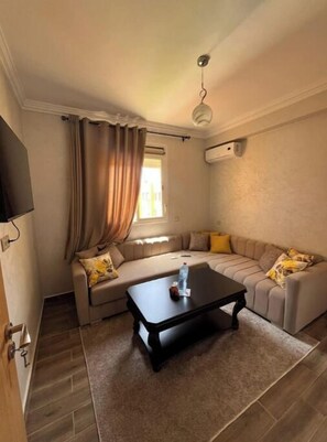 A living room with a sofa, a coffee table, a TV mounted on the wall, and a window with curtains. - Elegance & Serenity (Marrakech)