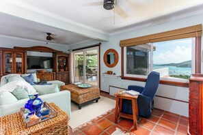 A living room with a television, sofa, coffee table, and a view of the sea. - East Gate In Coral Bay Back Up Power Included (Coral Bay)