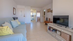 Een woonkamer met een bank, televisie en een tv-meubel met boeken en een afstandsbediening.