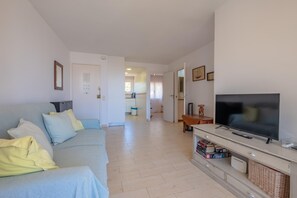 Un salon avec un canapé, un téléviseur et un meuble TV sur lequel sont posés des livres et une télécommande.