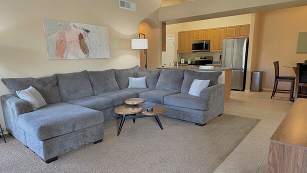 A living room with a grey sectional sofa, a coffee table, and a painting on the wall. - Heated Pools, King Bed, Fast Wi-Fi – Gated East Mesa 2BR Condo with Balcony (Mesa)
