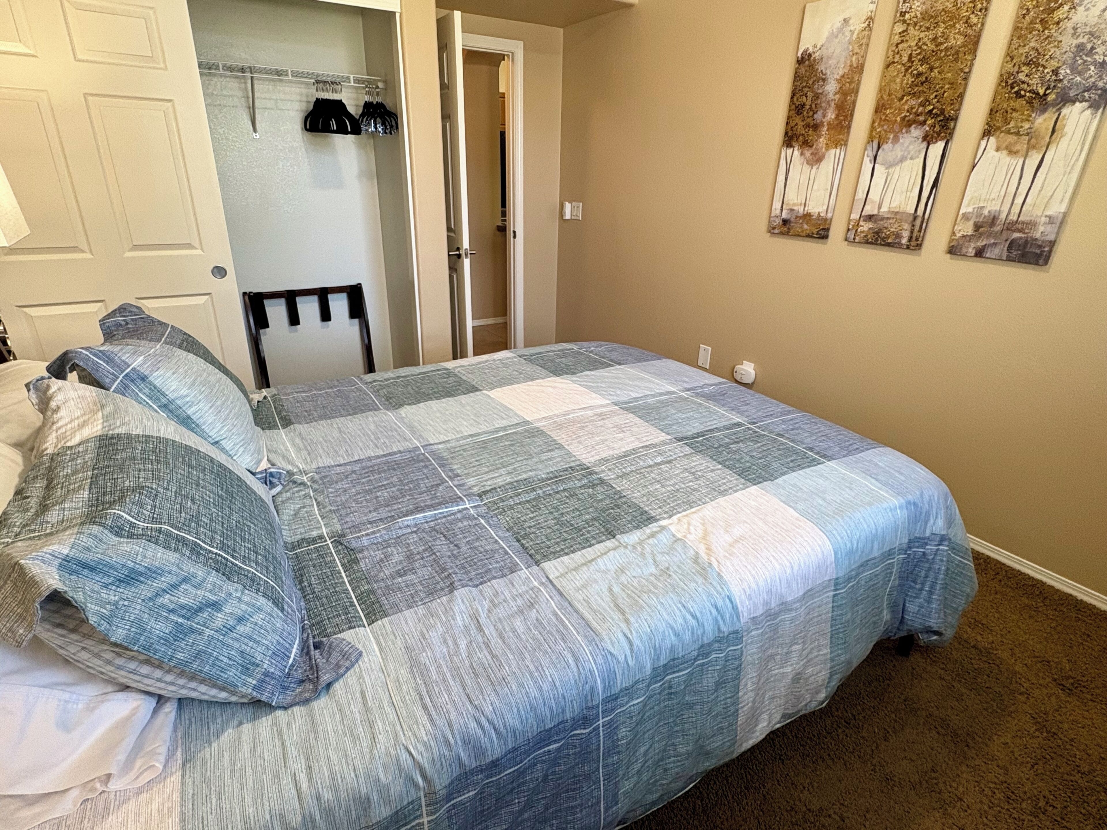 A bedroom with a bed, a door, a coat rack, and a wall with a painting.