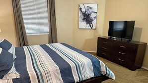 A bedroom with a bed, a TV on a dresser, a window with blinds, and a painting on the wall. - Heated Pools, King Bed, Fast Wi-Fi – Gated East Mesa 2BR Condo with Balcony (Mesa)