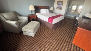 Ein Hotelzimmer mit Bett, Sessel, Schreibtisch, Nachttisch und Spiegel.