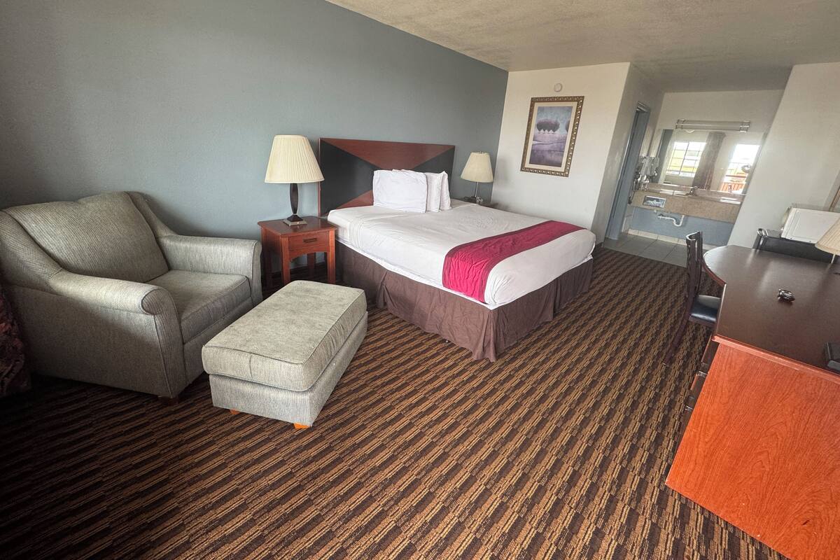 A hotel room with a bed, a chair, a desk, a nightstand, and a mirror.