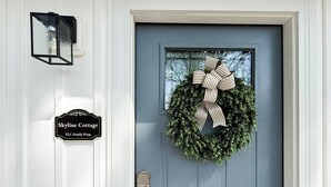 En dør med en krans, et skilt med teksten 'Skyline Cottage TLC Family Prop.' og en lanterne monteret på væggen.