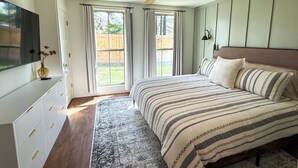 Et soveværelse med seng, ventilator, fjernsyn og et vindue med gardiner.