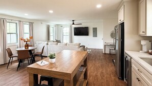 En rummelig opholdsstue med et træbord, en sofa og et køkken med moderne hårde hvidevarer.
