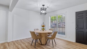 Een eethoek met een ronde tafel, vier stoelen, een hanglamp en een raam met jaloezieën.