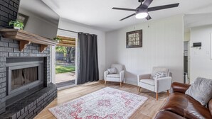 Een woonkamer met een open haard, twee fauteuils, een bruine leren bank, een plafondventilator en een kamerbreed tapijt.