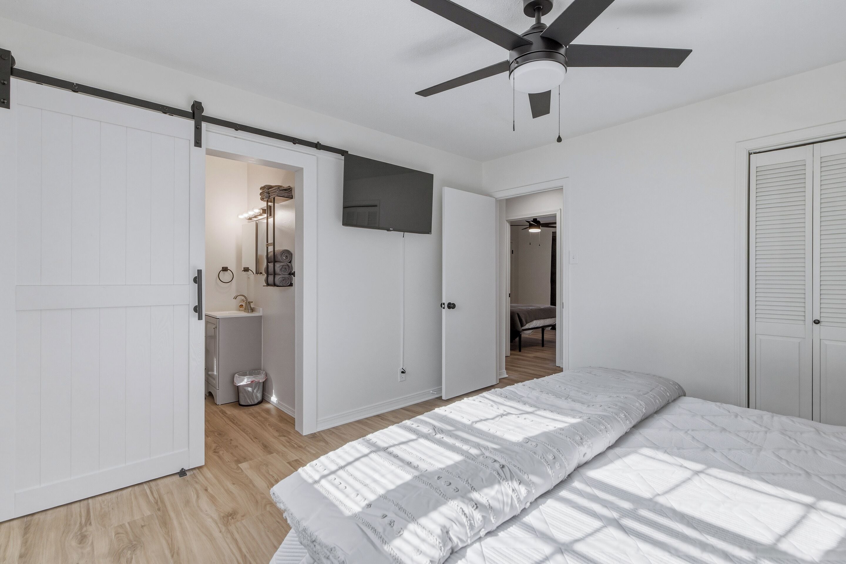 Une chambre à coucher comprenant un lit, un ventilateur de plafond, une télévision et une salle de bain avec un lavabo et un miroir.