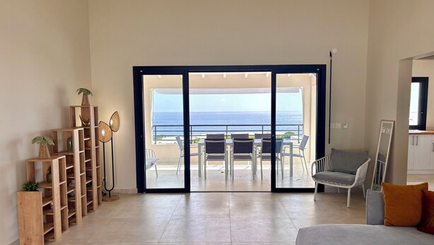 Un vaste espace de vie avec vue sur la mer, un balcon agrémenté de mobilier d’extérieur et une étagère en bois.