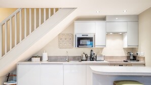 A modern kitchen with white cabinets, a built-in oven, and a wooden stool. - St Mary’s Mews - A Charming York Retreat (York)