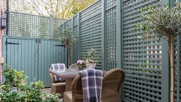 A patio with wicker furniture, a table, and a green fence. - St Mary’s Mews - A Charming York Retreat (York)