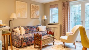 A living room with a sofa, a chair, a table, and a radiator. - St Mary’s Mews - A Charming York Retreat (York)