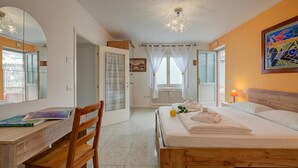A bedroom with a wooden bed, a desk with a chair, a mirror, and a window with curtains. - Vida Boa Apartment with Private Balcony Dining, Torbole sul Garda, Italy (Torbole sul Garda)