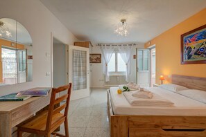 Ein Schlafzimmer mit einem hölzernen Bett, einem Schreibtisch mit Stuhl, einem Spiegel und einem Fenster mit Vorhängen.
