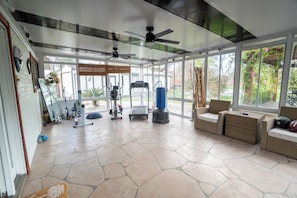 Una sala de estar con ventanales amplios, equipamiento de ejercicio y mobiliario de mimbre.