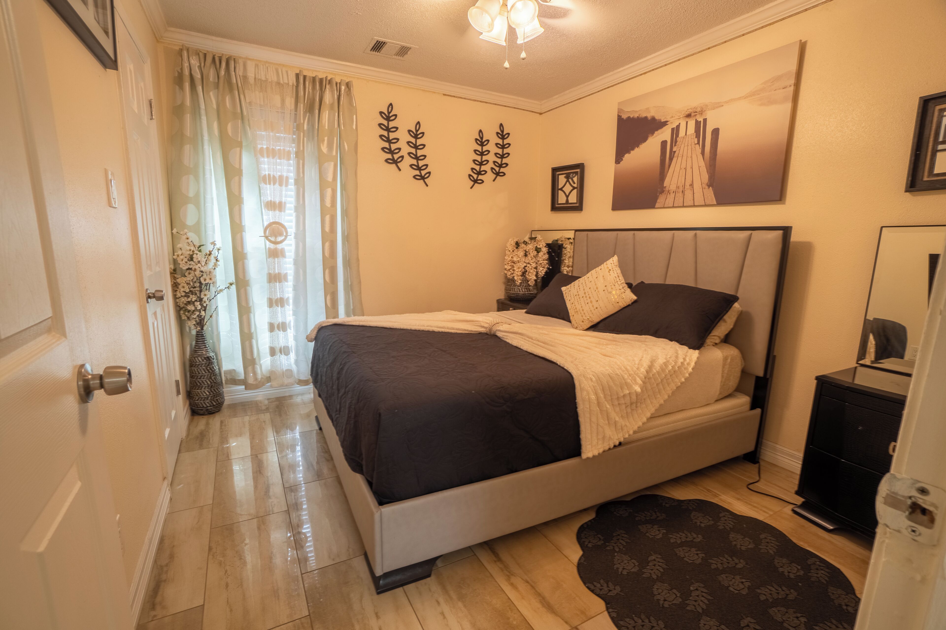 Camera da letto con un letto, un comodino, una cassettiera, uno specchio, una finestra con tende e decorazioni alle pareti.