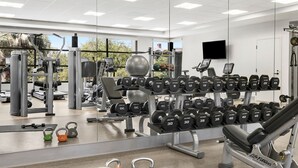 Et fitnesscenter med forskellig træningsudstyr, herunder håndvægte og kettlebells, samt et spejl der reflekterer rummet.