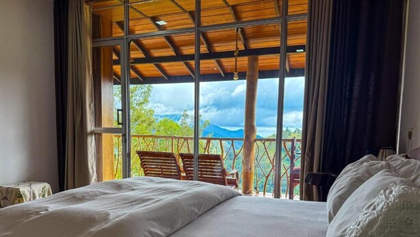 Une chambre avec un grand lit, un balcon avec des chaises et une vue sur l’extérieur.