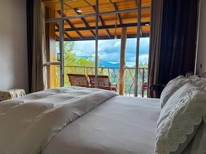 A bedroom with a large bed, a balcony with chairs, and a view of the outdoors. - Wooden Dream Ella (Ella)