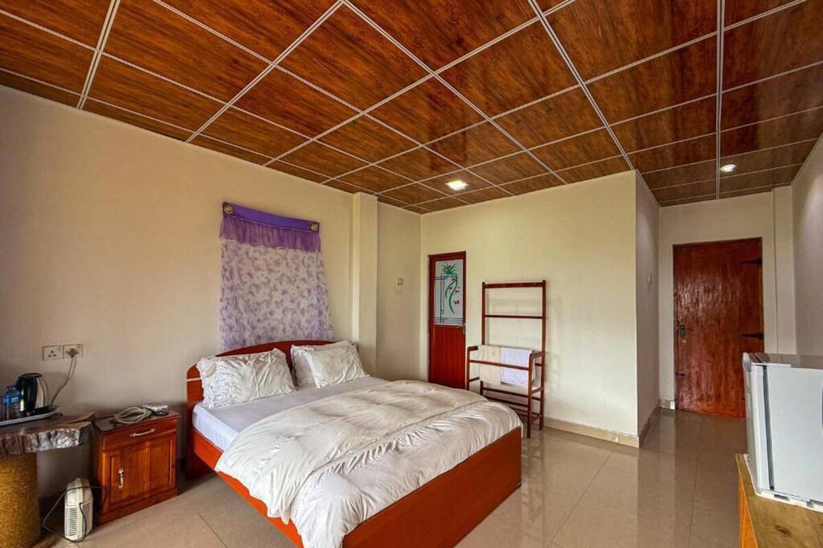Een slaapkamer met een houten plafond, een bed, een nachtkastje met een lamp, een tv-meubel en een kledingkast.