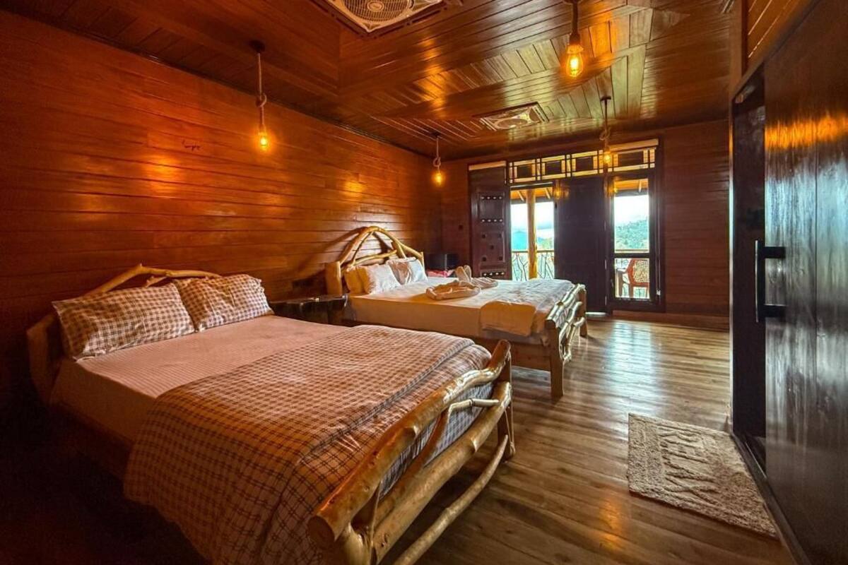Een houten kamer in chaletstijl met twee bedden, een groot raam en een plafondventilator.