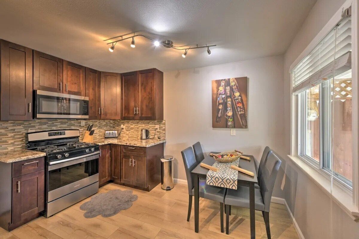 A kitchen with wooden cabinets, a stainless steel stove, a microwave, and a dining area with a table and chairs.