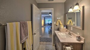 A bathroom with a sink, mirror, towel rack, and a view into the living area. - Silver Modern 2BR: Pet-Friendly Oasis w/ Fenced Private Garden Near Downtown (Carmichael)