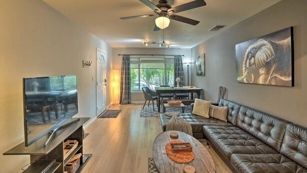 A living room with a flat-screen TV, a leather sofa, a coffee table, a ceiling fan, and a dining area with a table and chairs. - Silver Modern 2BR: Pet-Friendly Oasis w/ Fenced Private Garden Near Downtown (Carmichael)