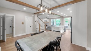 A spacious dining area with a long table and chairs, a staircase, and a kitchen in the background. - 4BR Near The Woodlands | Quiet Neighborhood | King Suite | Pet Friendly (Conroe)