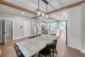 A spacious dining area with a long table and chairs, a staircase, and a kitchen in the background. - 4BR Near The Woodlands | Quiet Neighborhood | King Suite | Pet Friendly (Conroe)