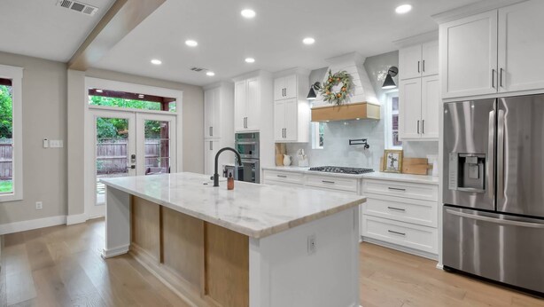 A modern kitchen with white cabinetry, a large island, stainless steel appliances, and a view to the outdoors. - 4BR Near The Woodlands | Quiet Neighborhood | King Suite | Pet Friendly (Conroe)