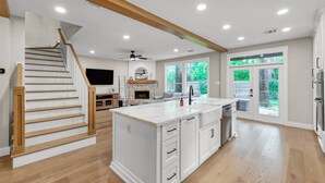 A spacious kitchen with a central island, a dining area with a sofa, a fireplace, and a staircase leading to another level. - 4BR Near The Woodlands | Quiet Neighborhood | King Suite | Pet Friendly (Conroe)