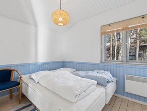 Een slaapkamer met een bed, een stoel, een hanglamp, een raam met uitzicht op bomen en een radiator.