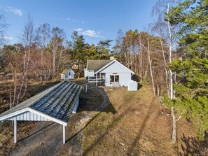 Een chalet met een schuin dak, een veranda en een kleine schuur in een bebost gebied.
