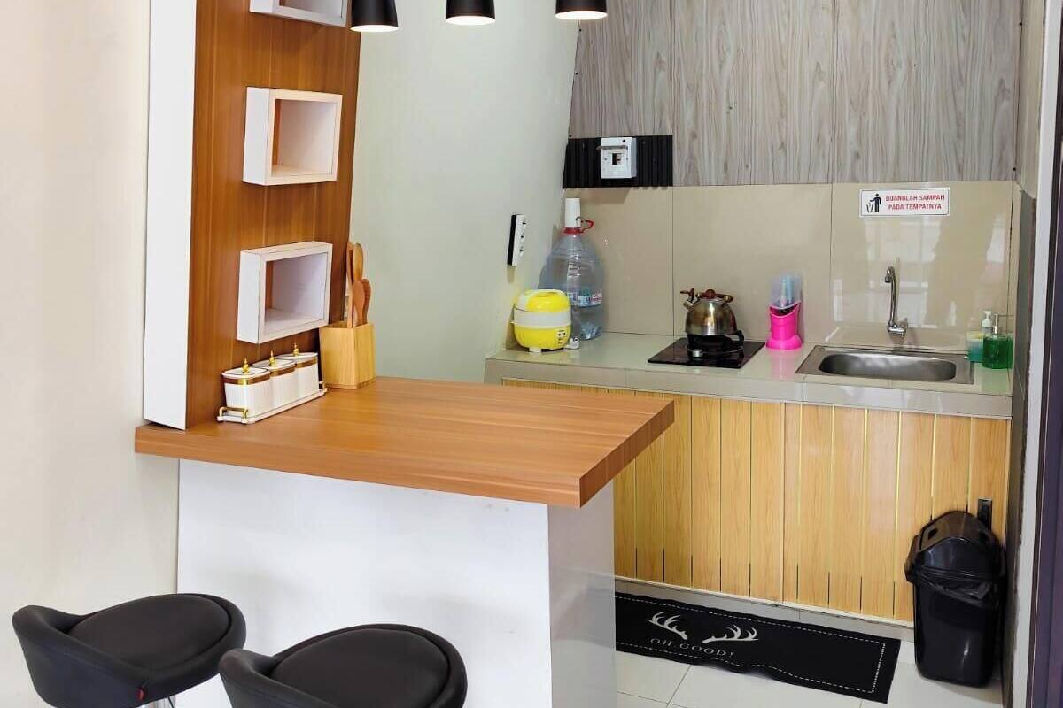 Una cocina compacta con encimera de madera, dos taburetes negros, un lavamanos y un refrigerador pequeño.
