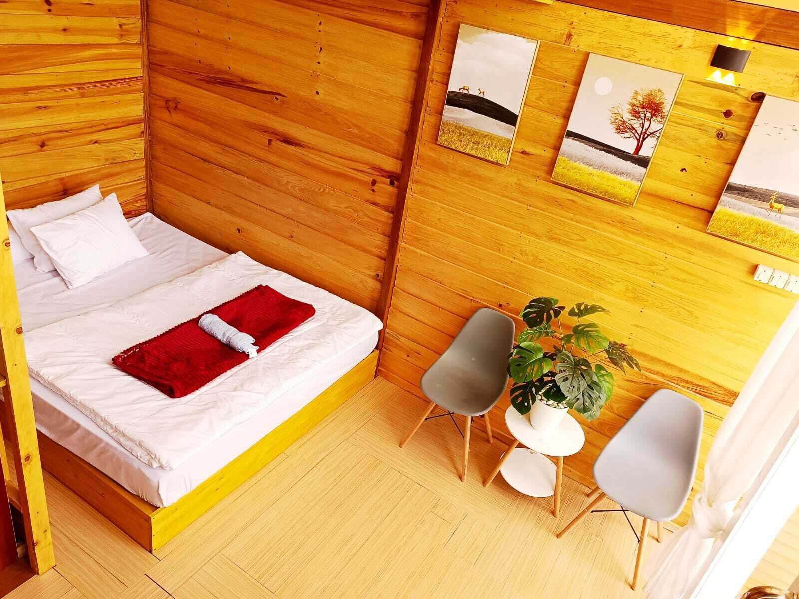 Una habitación de madera con una cama, dos sillas, una mesita y una planta en maceta.